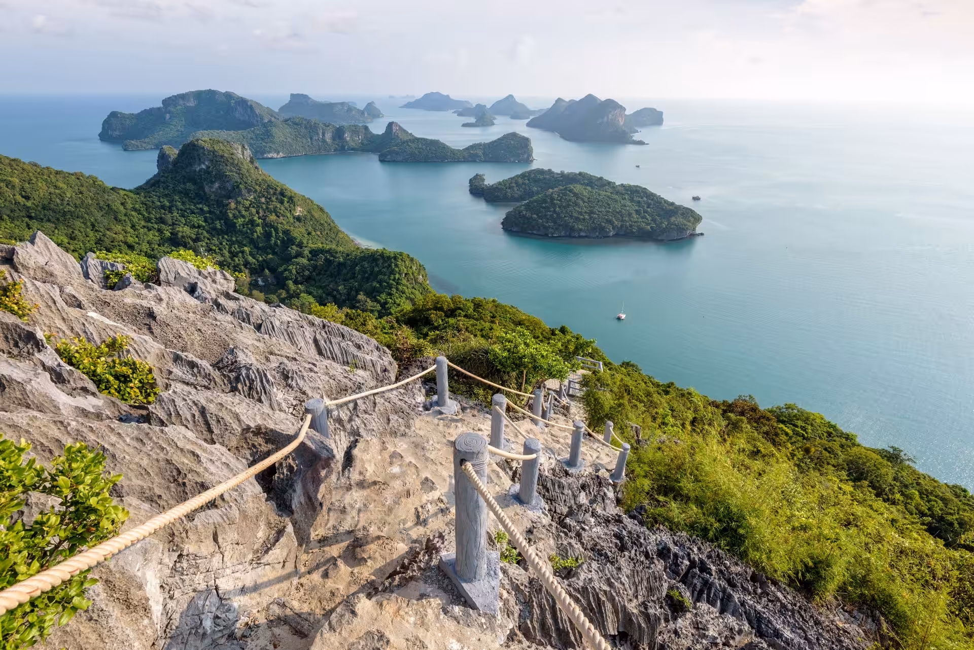Rocky hillside with a pathway leading down to a serene bay dotted with islands and greenery.